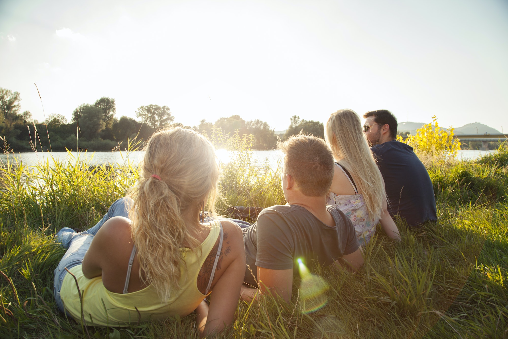 Four young adult friends reclining on riverbank